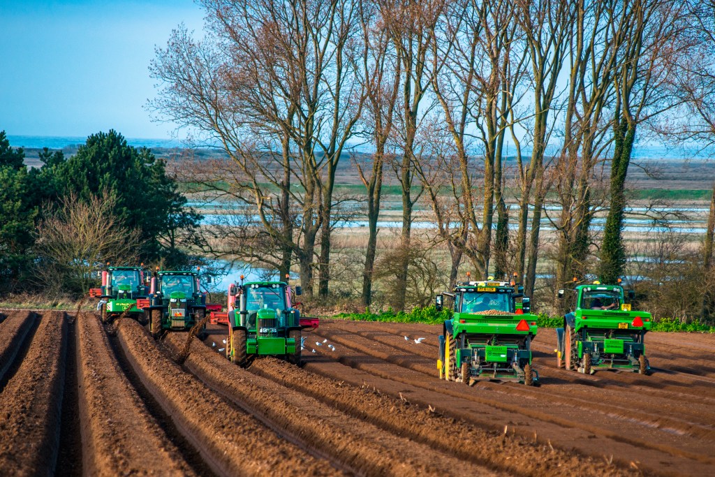 five green John Deere tractors preparing a large field for planting