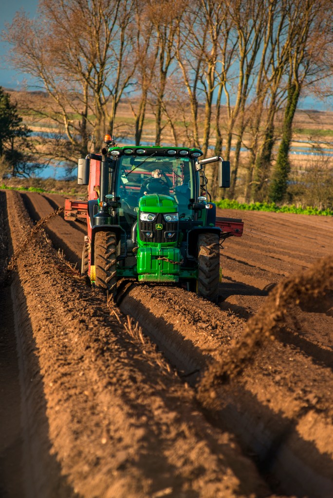 a John Deere tractor is shaping rows with a bed shaper in a large unplanted crop field
