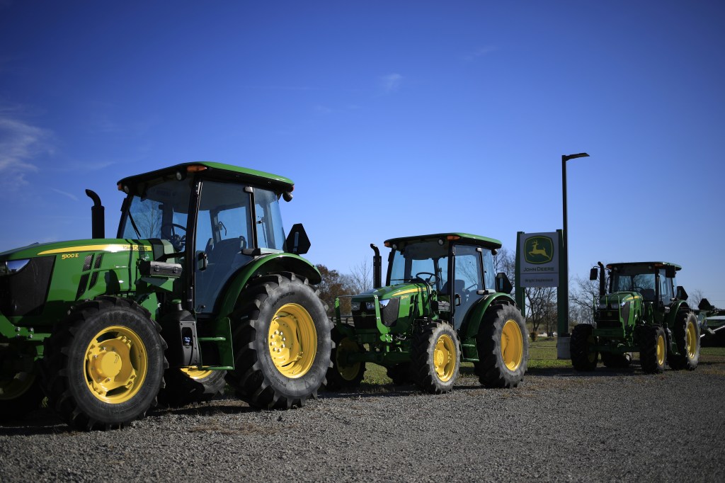 a lineup of green John Deere tractors at a dealership in front of a John Deere sign
