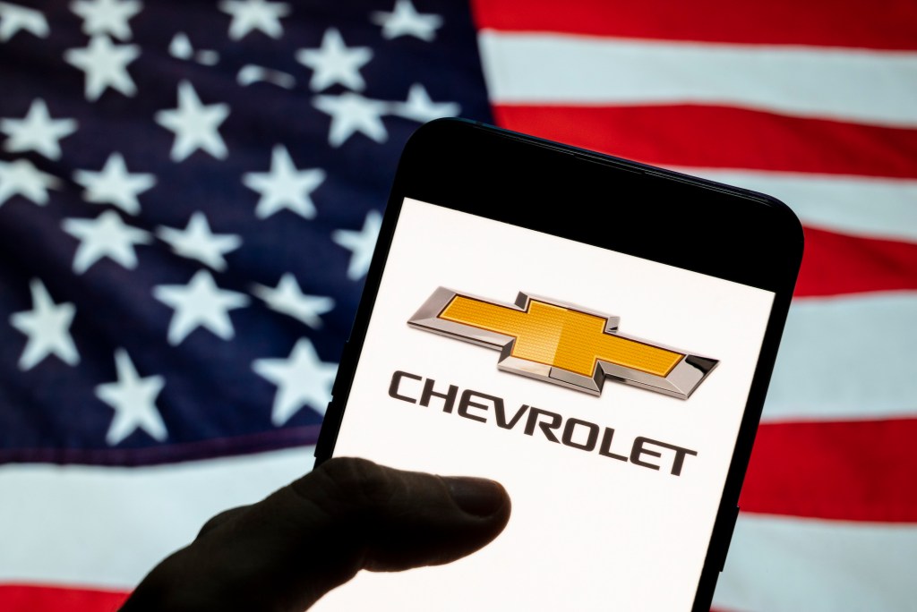 Chevrolet logo seen displayed on a smartphone with a flag of the United States in the background