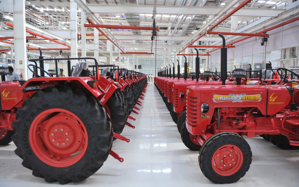 a line of red Mahindra Tractors fresh off the line in a manufacturing facility 
