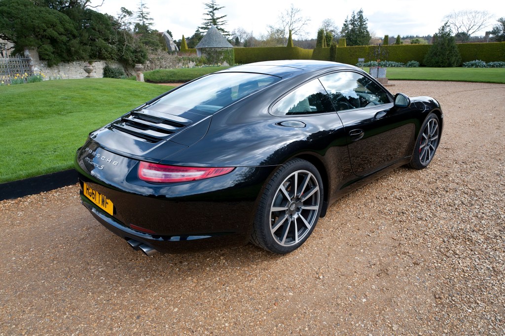The rear of a Porsche 911 in black on a gravel driveway