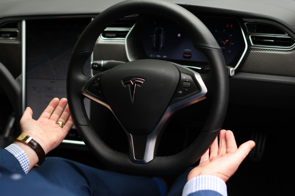 A man removes his hands from the steering wheel of a Tesla on Autopilot