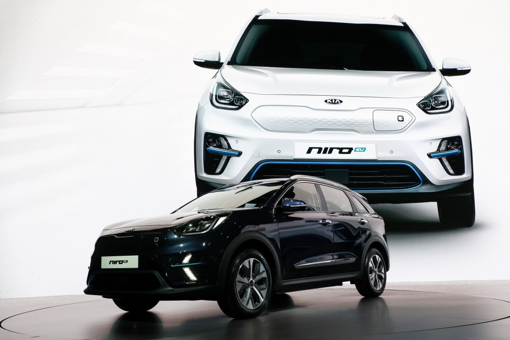 A Kia Niro EV at a press launch with a large image of the car on a screen in the background.