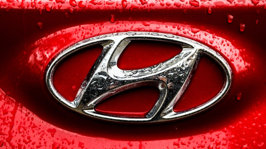 A silver Hyundai emblem on a red car is covered with raindrops