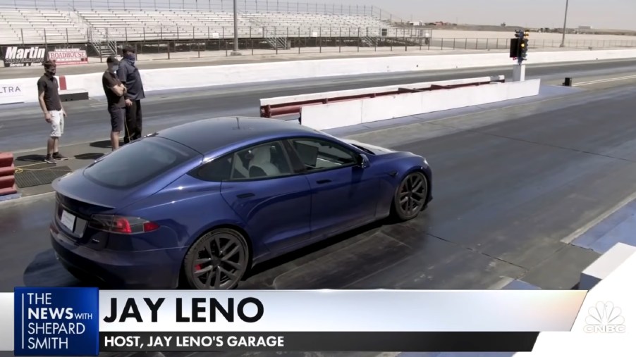 NHRA officials look on as Jay Leno sits on a dragstrip in a blue Tesla Model S Plaid
