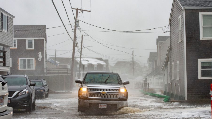 A truck drives through a flooded street as waves crash over the sea walls during high tide in a winter storm in Scituate, Massachusetts