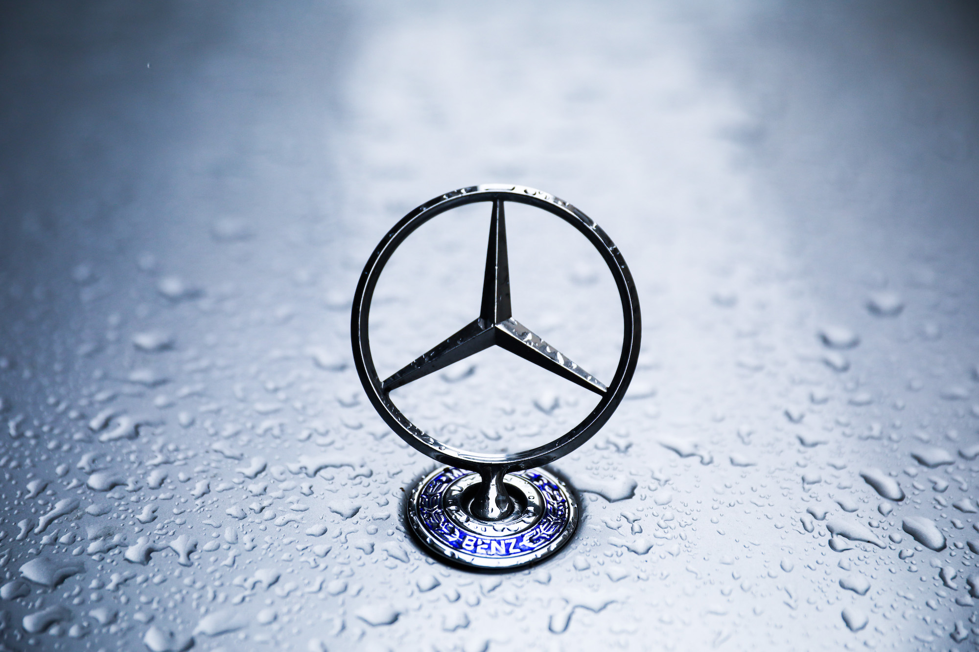 A silver Mercedes-Benz emblem on a vehicle's hood covered in raindrops