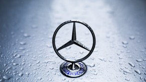 A silver Mercedes-Benz emblem on a vehicle's hood covered in raindrops