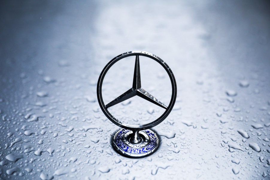 A silver Mercedes-Benz emblem on a vehicle's hood covered in raindrops