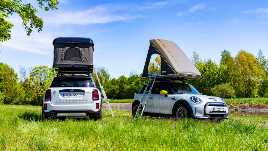 Parked in a field, a white Mini Cooper Countryman and a white Mini Cooper hold rooftop tents
