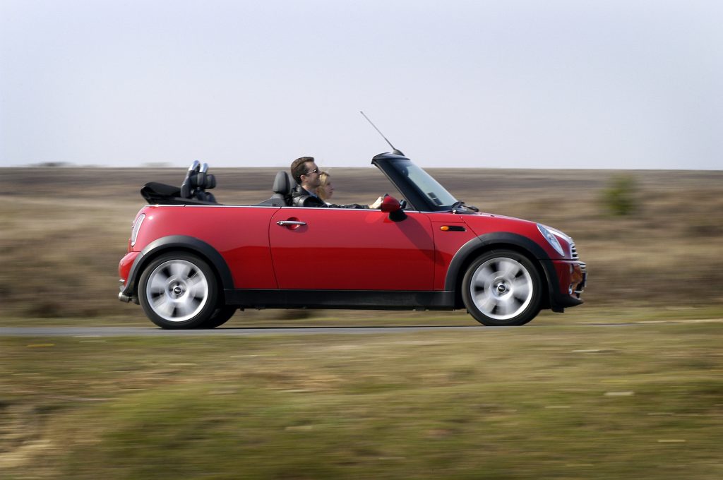 A Mini Cooper Convertible driving down the road