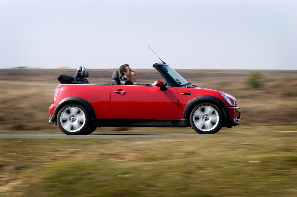 A Mini Cooper Convertible driving down the road