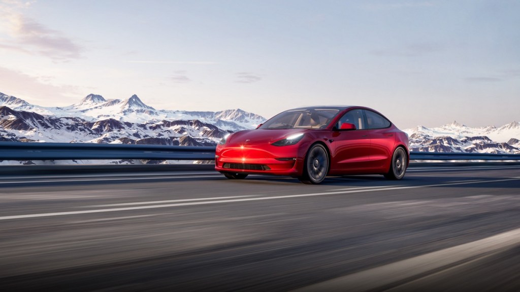 A red Tesla Model 3 driving on the highway.