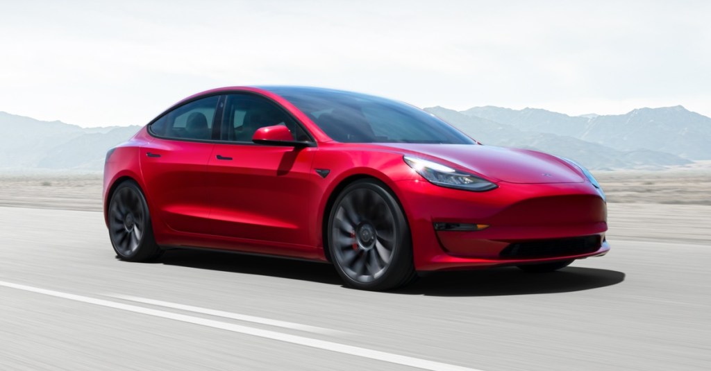 A red Tesla Model 3 drives down a highway.