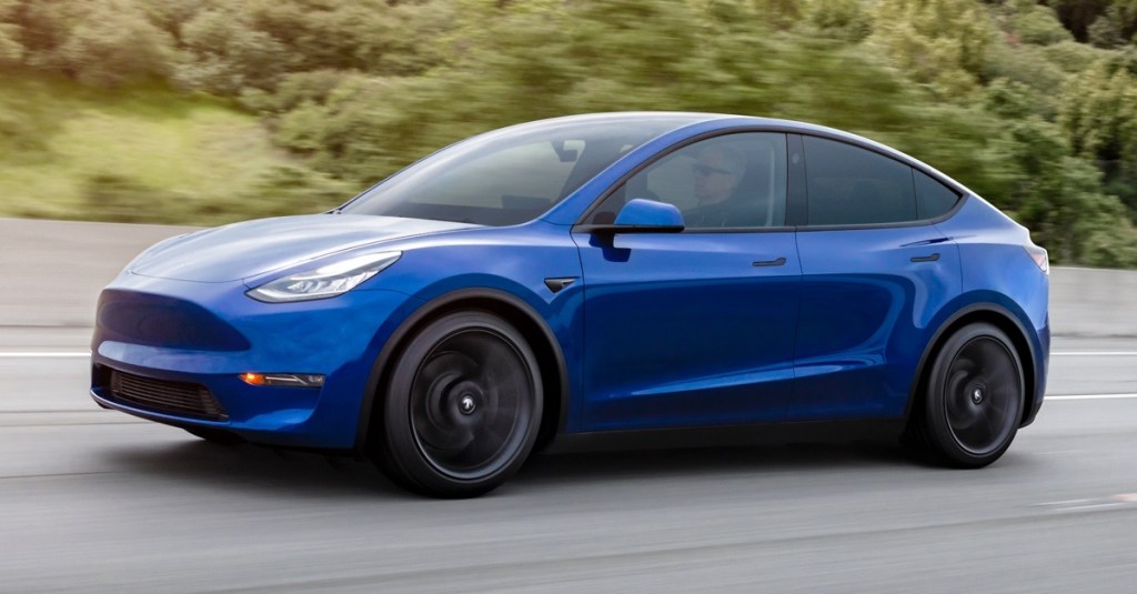 A blue Tesla Model Y drives down a road. 