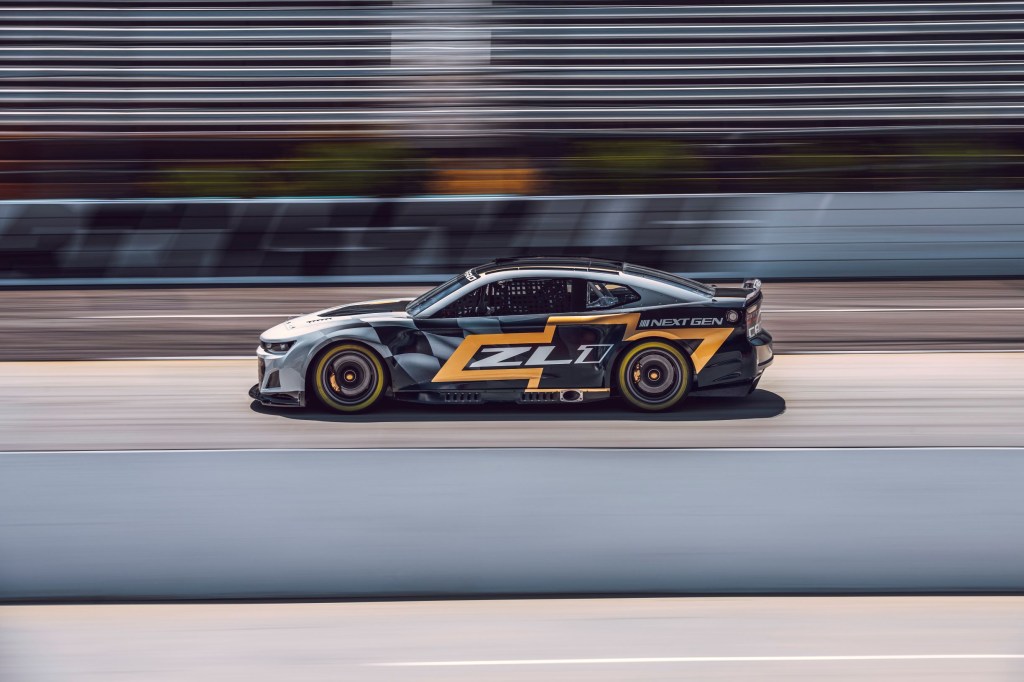 The side view of the silver-black-and-gold NASCAR Next Gen Chevrolet Camaro ZL1 speeding down a racetrack