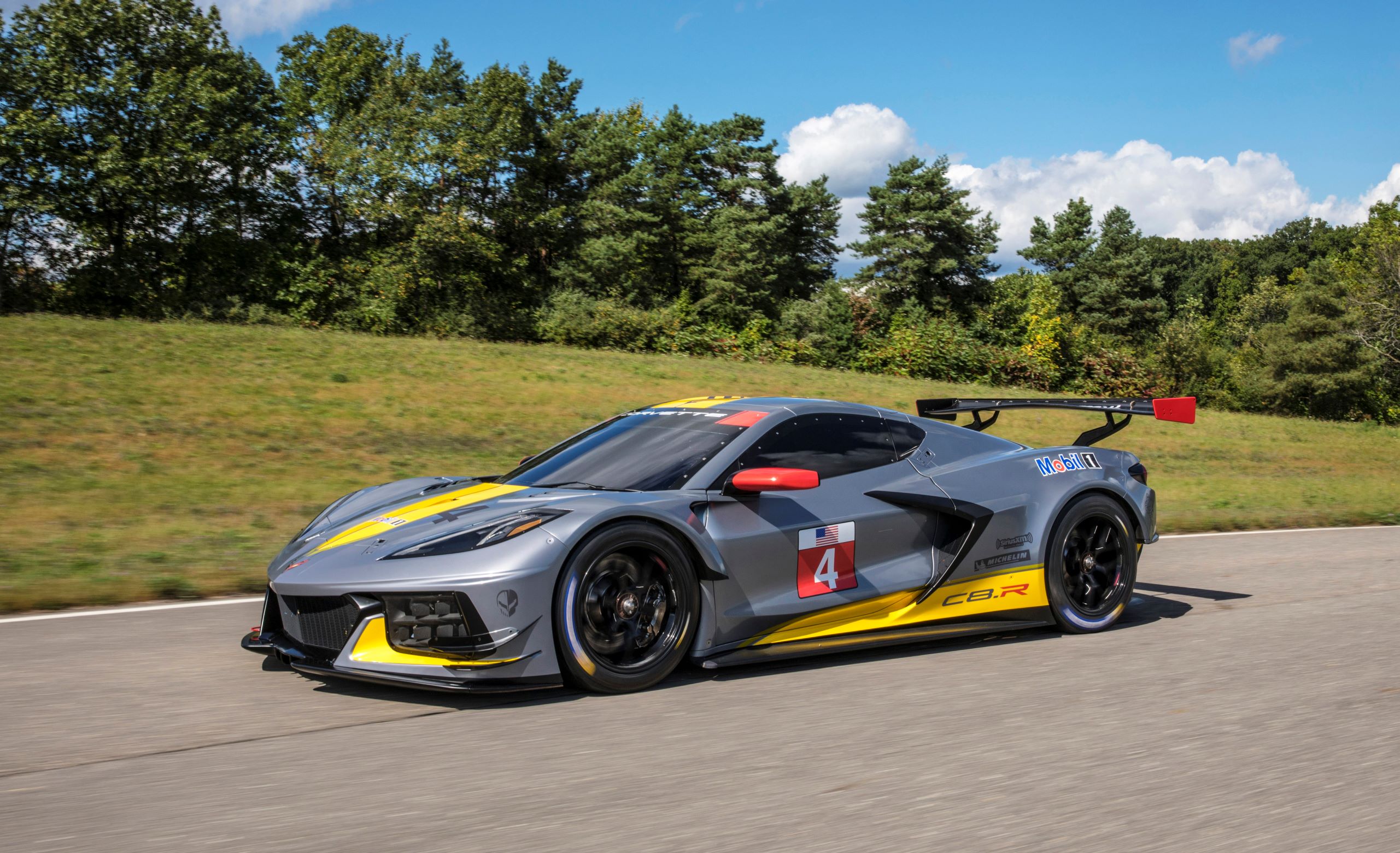 The gray-and-yellow No. 4 Chevrolet Corvette C8.R driving on a tree-line road