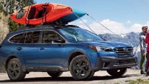 A blue 2021 Subaru Outback parked on a mountain with a couple and their dog standing nearby.