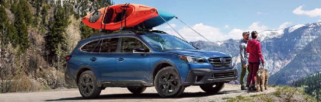 A blue 2021 Subaru Outback parked on a mountain with a couple and their dog standing nearby.