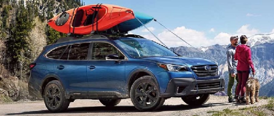 A blue 2021 Subaru Outback parked on a mountain with a couple and their dog standing nearby.