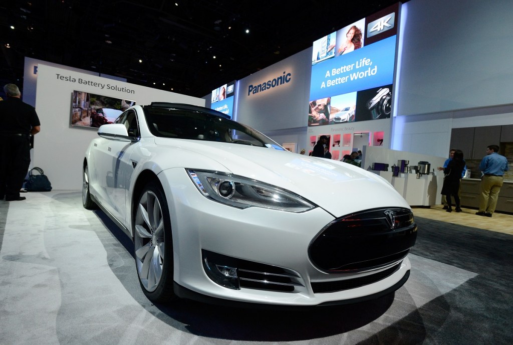 A white Tesla electric car on display at a Panasonic booth at a car show.  