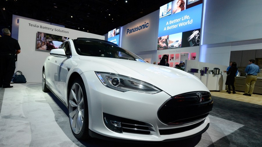 A white Tesla electric car on display at a Panasonic booth at a car show.
