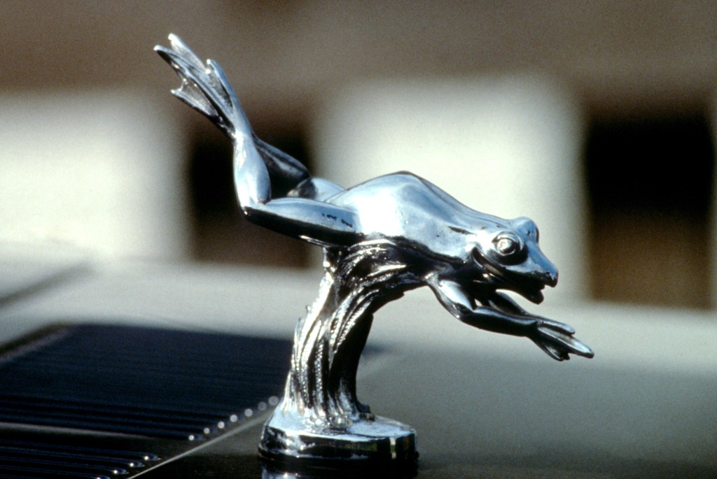 A silver hood ornament of a frog leaping forward as if diving into a pond