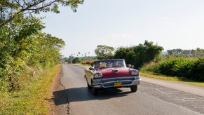 A red classic car driving down the street