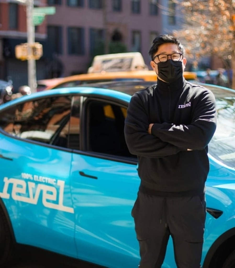 A Revel driver stands outside a blue Tesla Model Y Revel taxi.