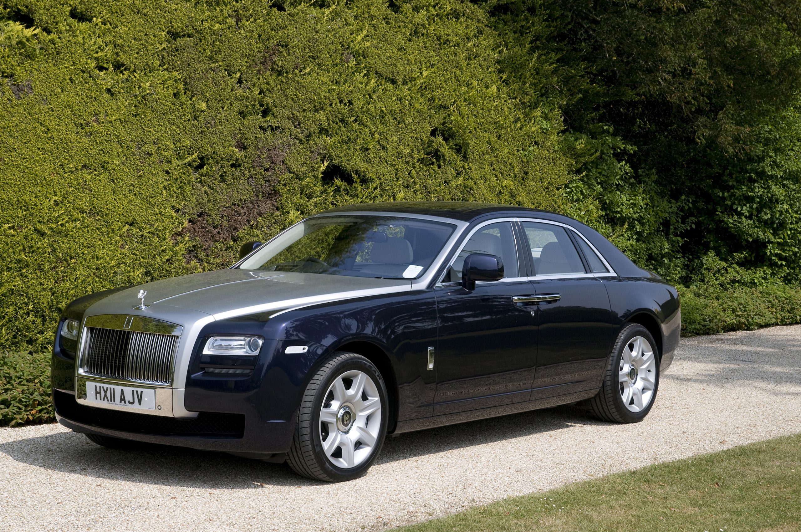 A black and silver Rolls-Royce Ghost luxury sedan parked in front of a tall hedge