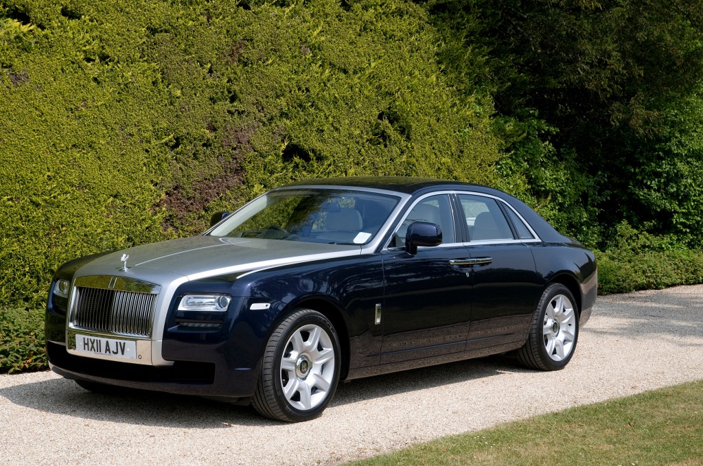A black and silver Rolls-Royce Ghost luxury sedan parked in front of a tall hedge