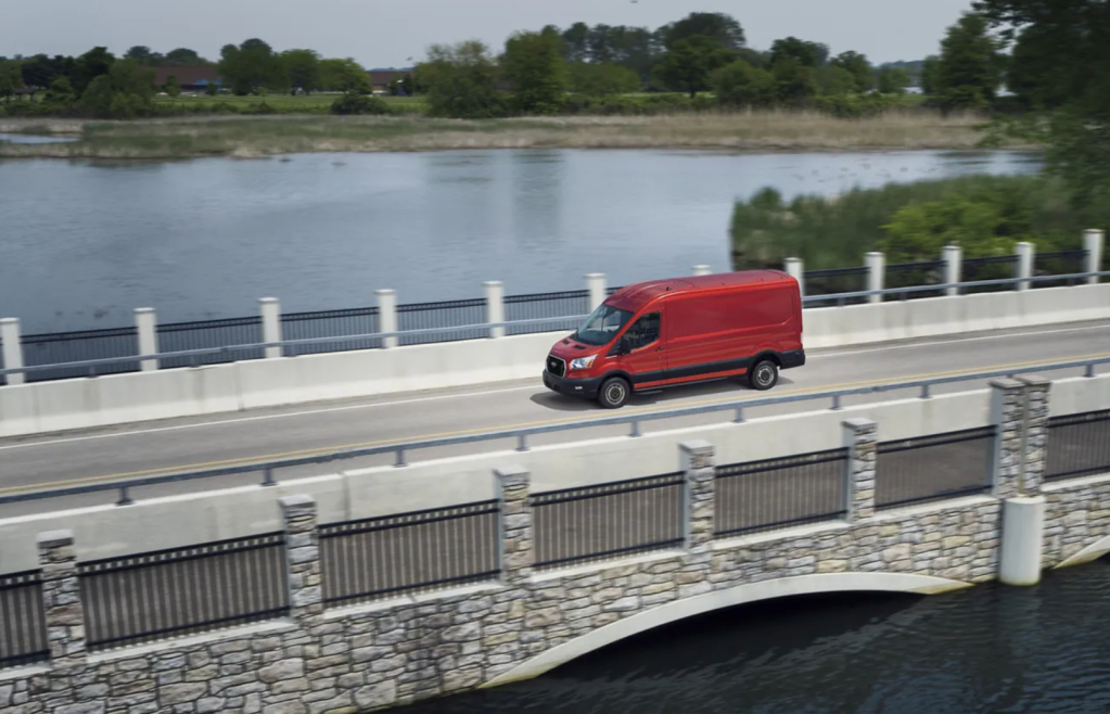 A red 2021 Ford Transit van driving over a bridge 