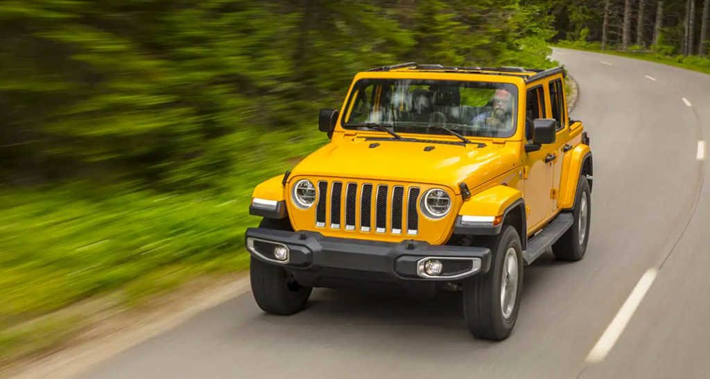 A yellow 2021 Jeep Wrangler driving down a forrest road 