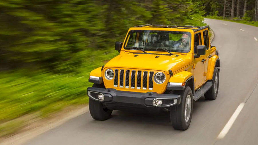A yellow 2021 Jeep Wrangler driving on a road in the woods