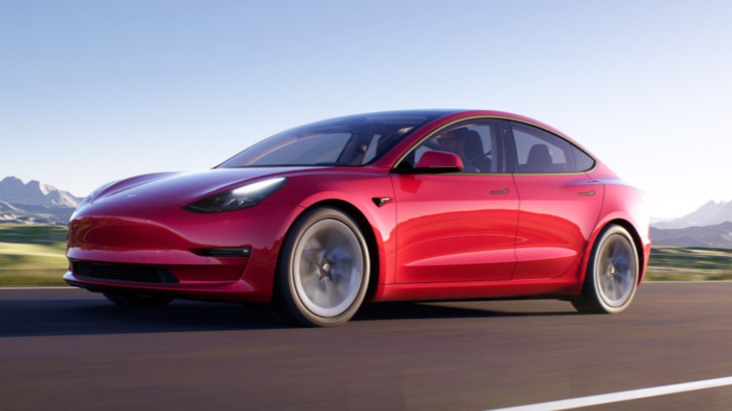 An image of a red Tesla Model 3 out on the road.