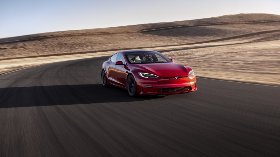A red Tesla Model S Plaid sedan drives on a curving road in a desert