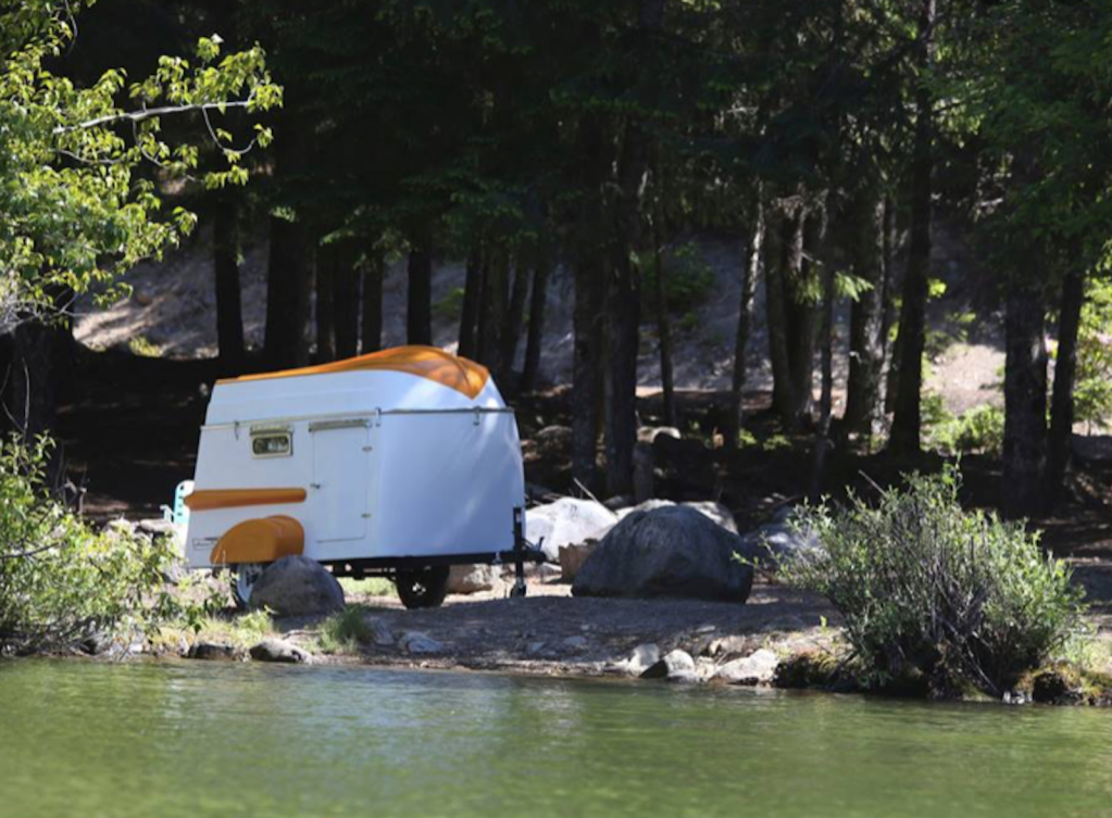 an orange and white boat trailer parked by the shore in a wooded area 