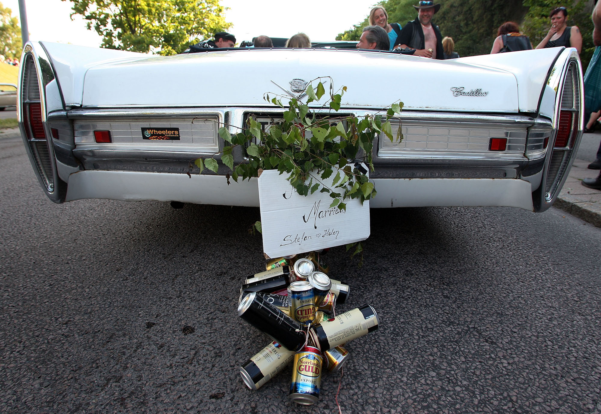 Beer cans hang under a 'Just Married' sign on a white Cadilllac wedding car