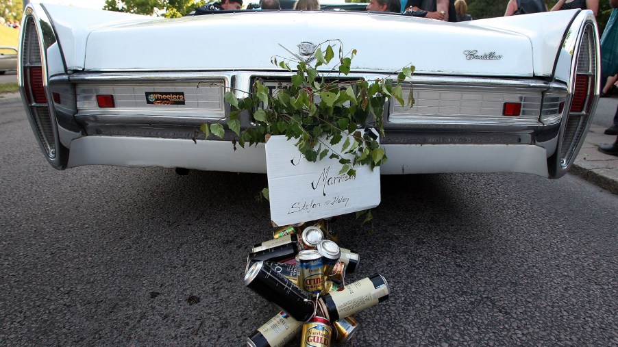 Beer cans hang under a 'Just Married' sign on a white Cadilllac wedding car