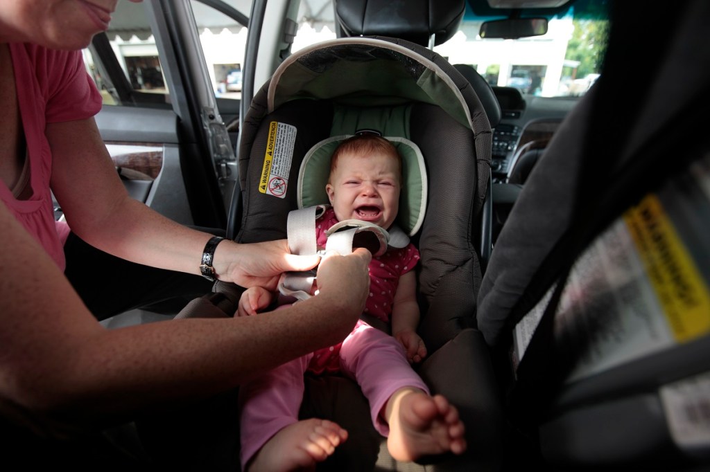 A crying baby strapped into a car seat.