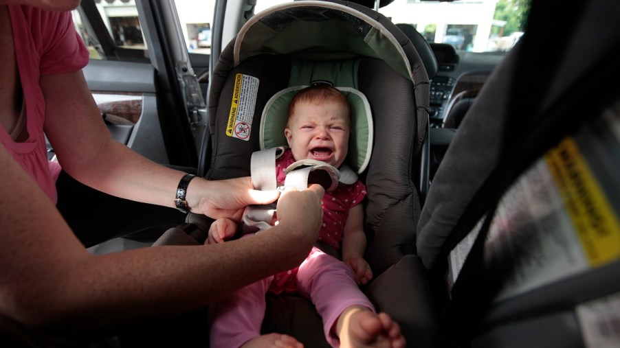 A crying baby strapped into a car seat.