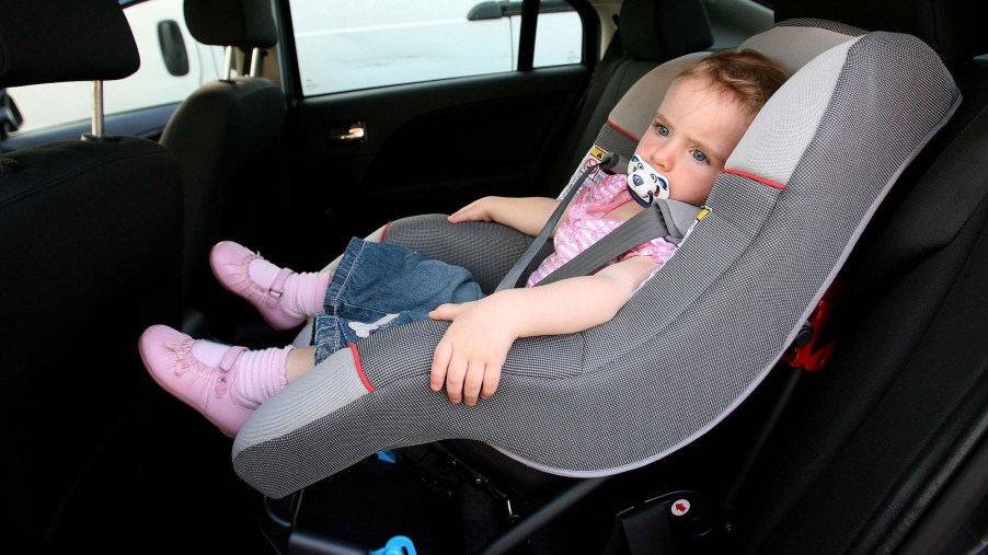 A small child in a foward-facing car seat in a vehicle's backseat