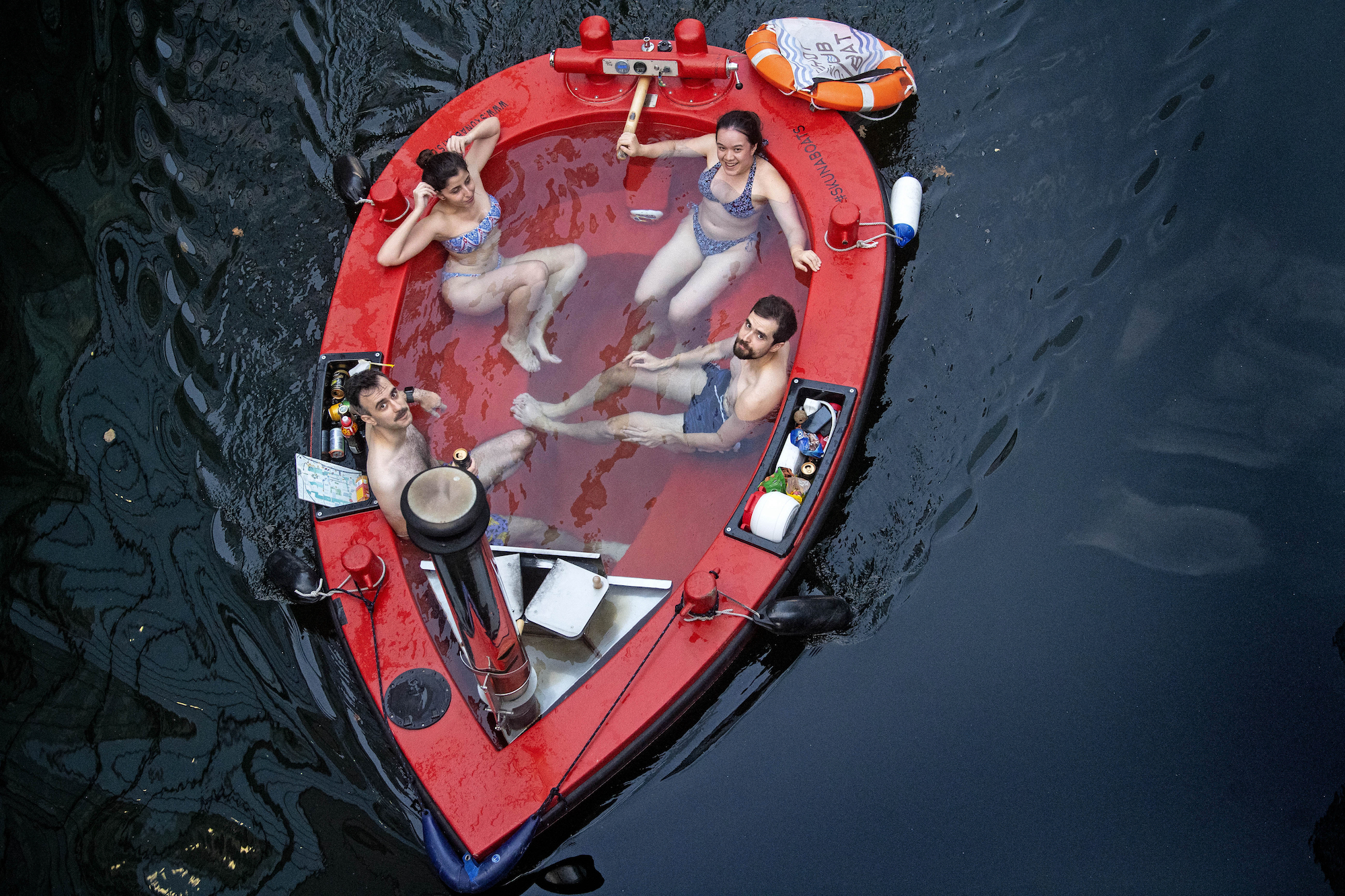 Four people sit inside a red hot tub boat
