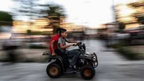 Two kids without helmets ride an ATV