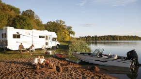 an RV camper and a small boat camping set up next to a lake