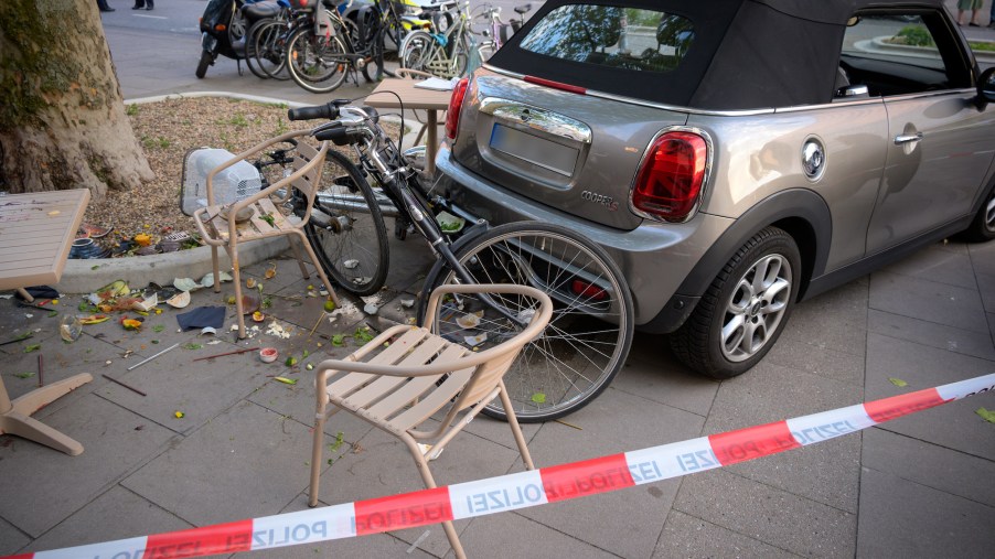 A rental car involved in an accident is parked among bicycles, tables, chairs and destroyed crockery