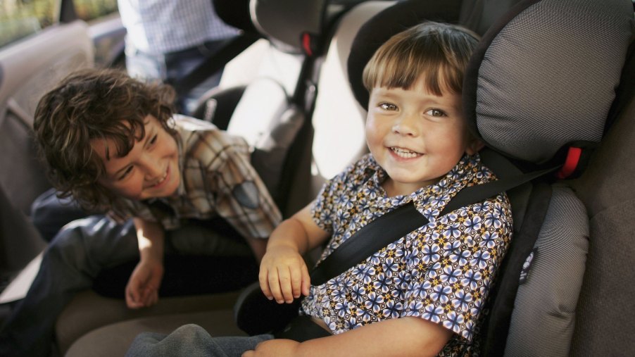Two young children sit in car seats in the backseat of a vehicle