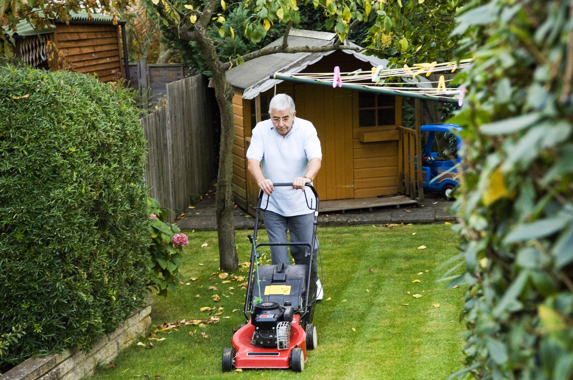 A man uses a walk-behind lawn mower in a backyard