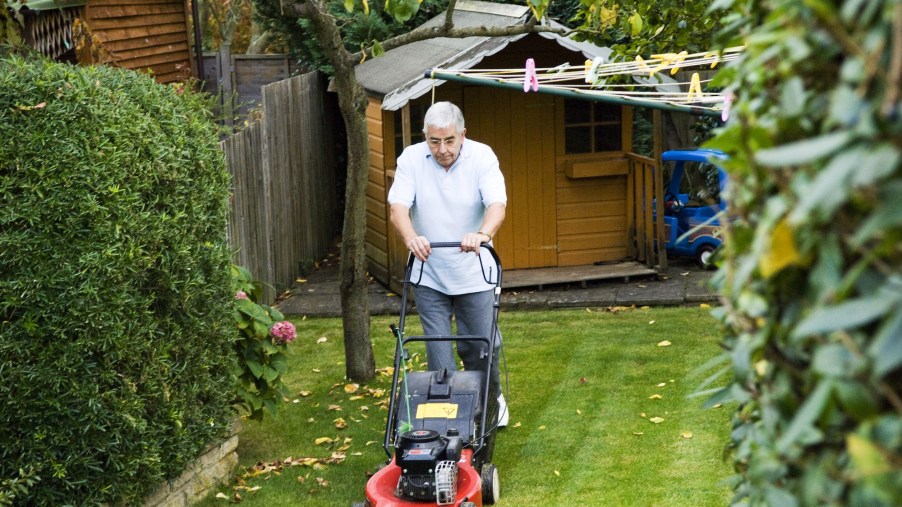 A man uses a walk-behind lawn mower in a backyard